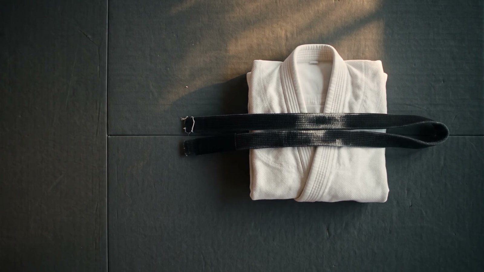 A worn black belt resting on a folded white gi in morning light