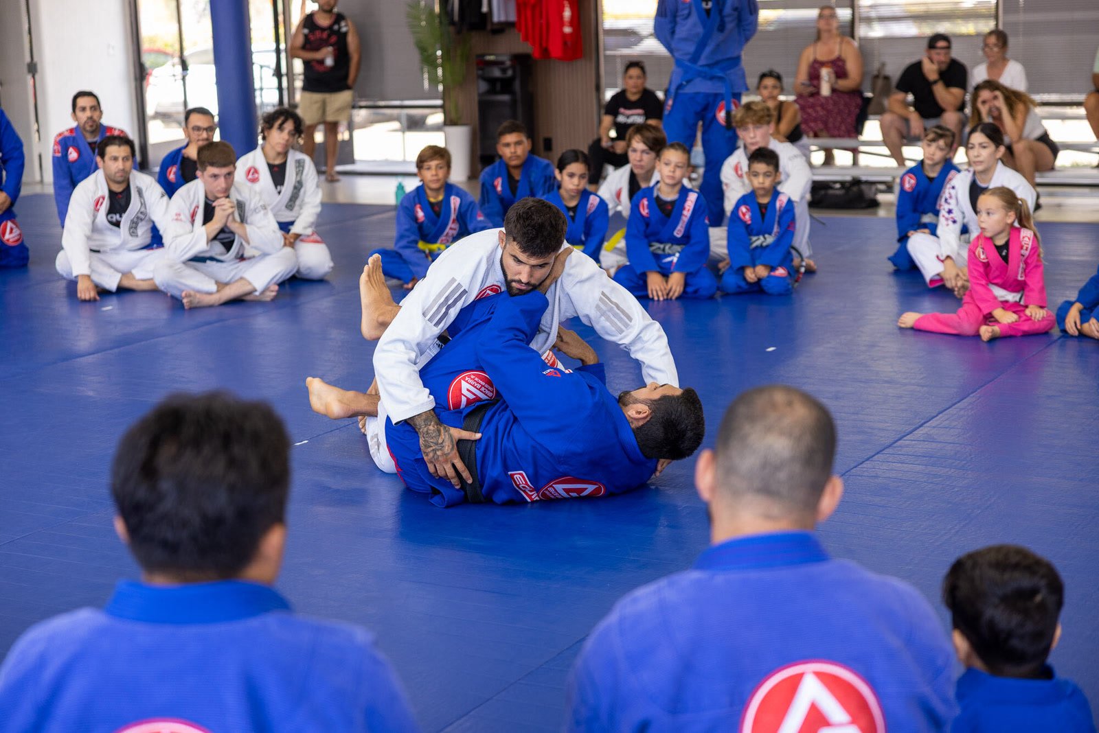 An instructor demonstrating a technique on the mat while students and parents watch